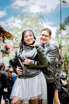 Happy couple in leather jackets posing outdoors, celebrating with bouquets and smiles.