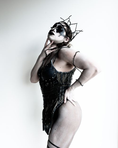 Free A person in dark, artistic cosplay with face paint and a crown poses dramatically against a white background. Stock Photo