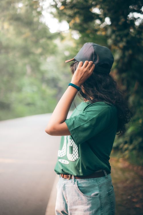 Free Casual young woman adjusting cap in lush outdoor setting, summer vibe. Stock Photo