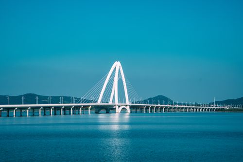 Free A contemporary cable-stayed bridge spanning serene blue water under clear skies. Stock Photo