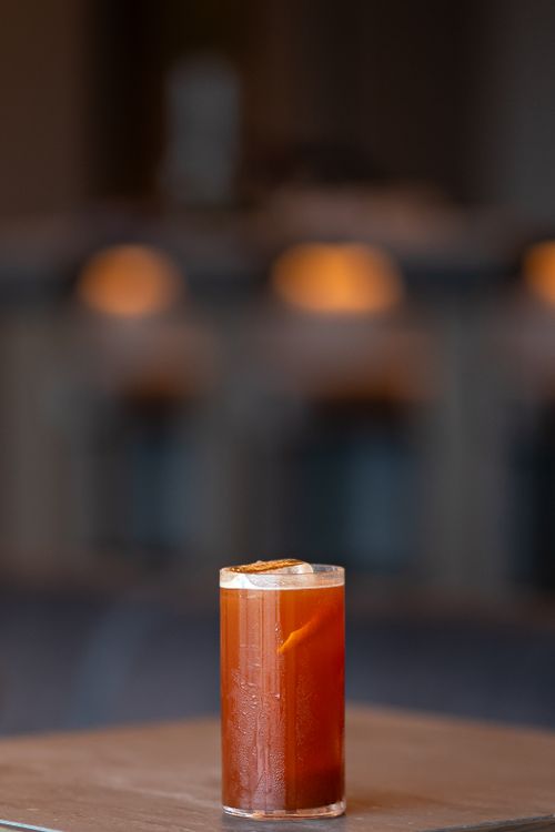 Free A chilled orange cocktail with a slice garnish on a table, set against a moody blurred background. Stock Photo