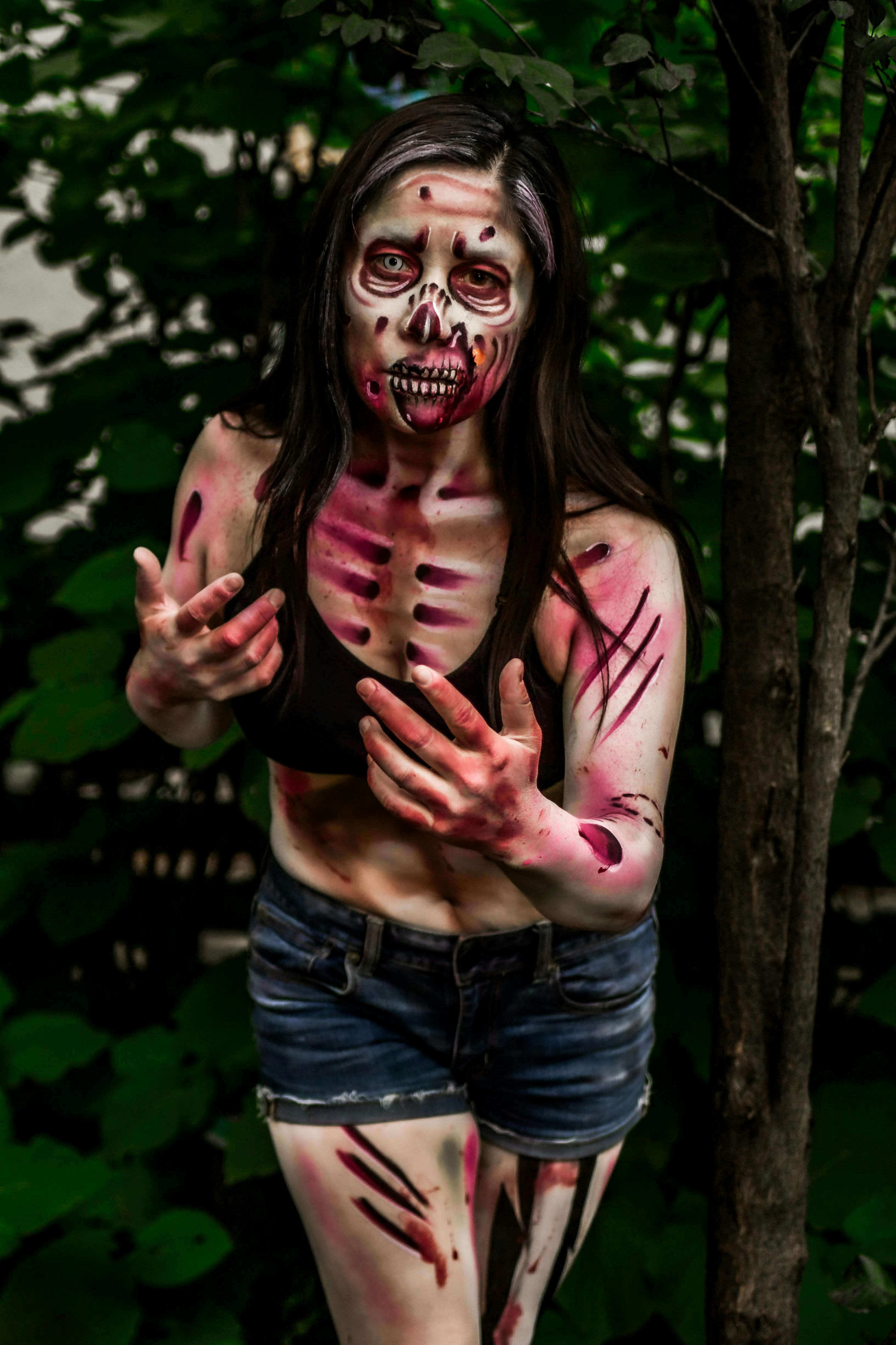 A person in a detailed zombie costume with special effects makeup standing in a forest.