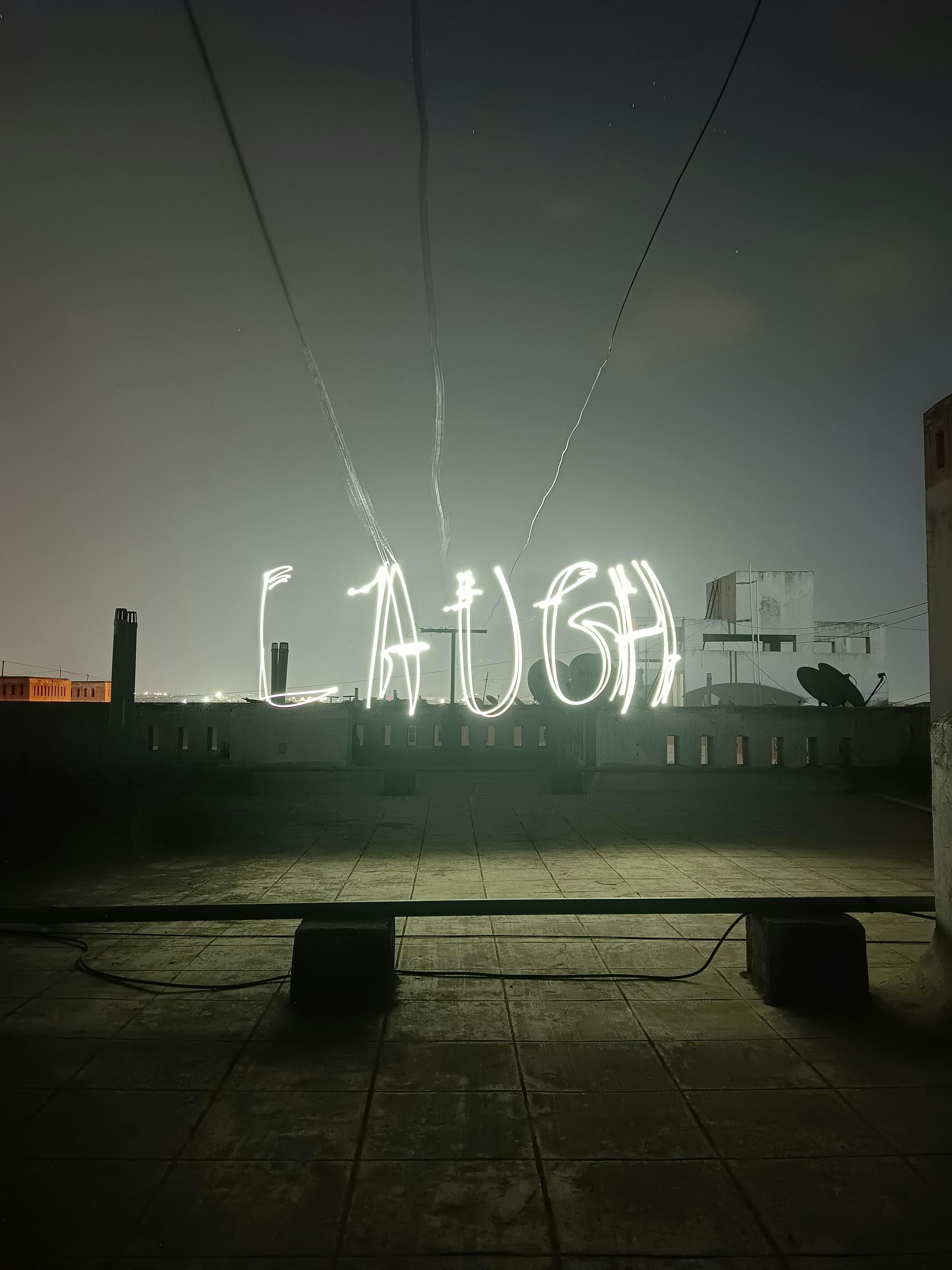 Captivating rooftop light painting showcasing the word "Laugh" against a night sky.