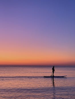 立陶宛奈达的日落充满活力，平静的水面上映出一名桨板者宁静的轮廓