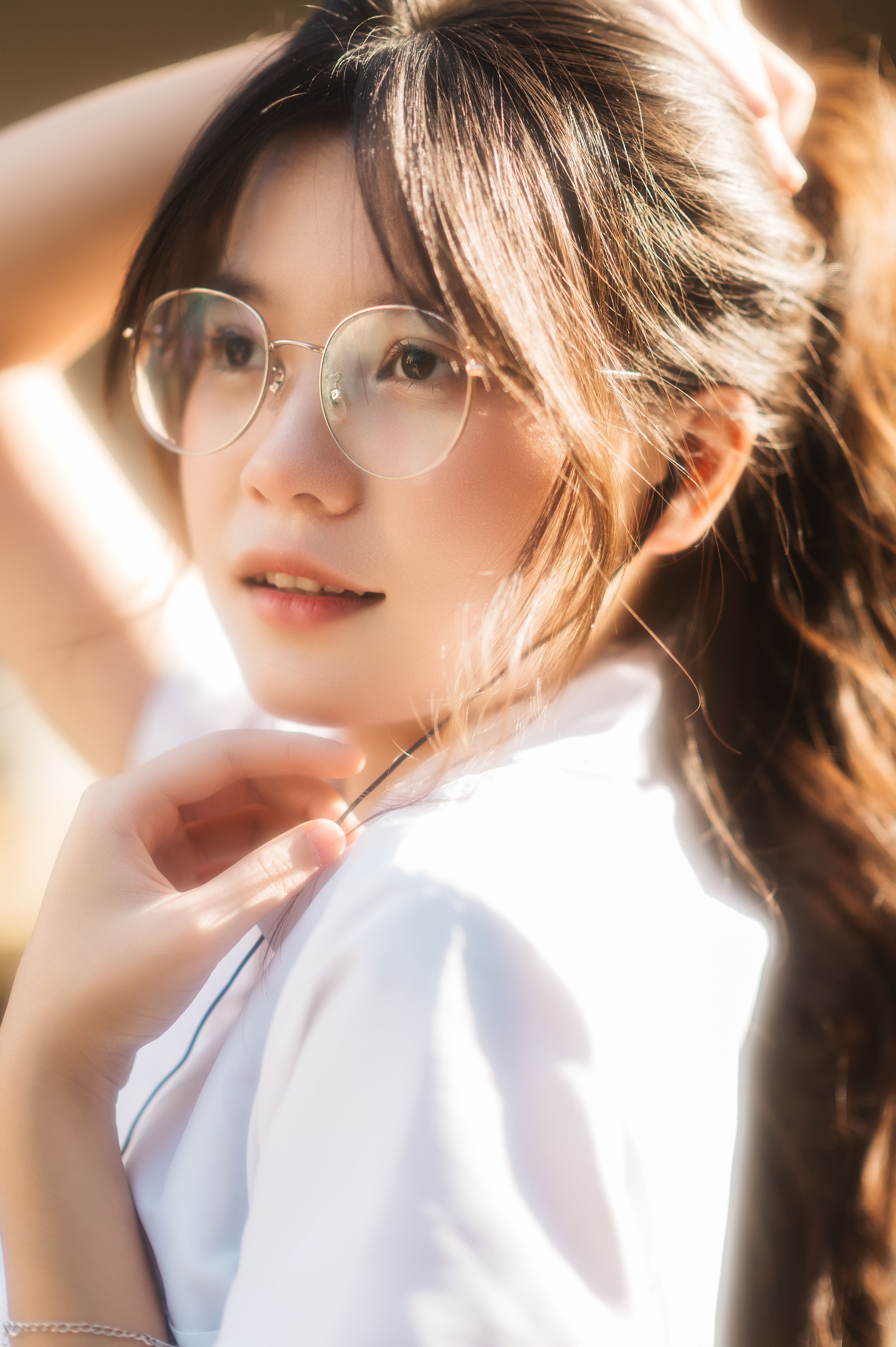 Close-up portrait of a young woman with glasses smiling in natural light outdoors.