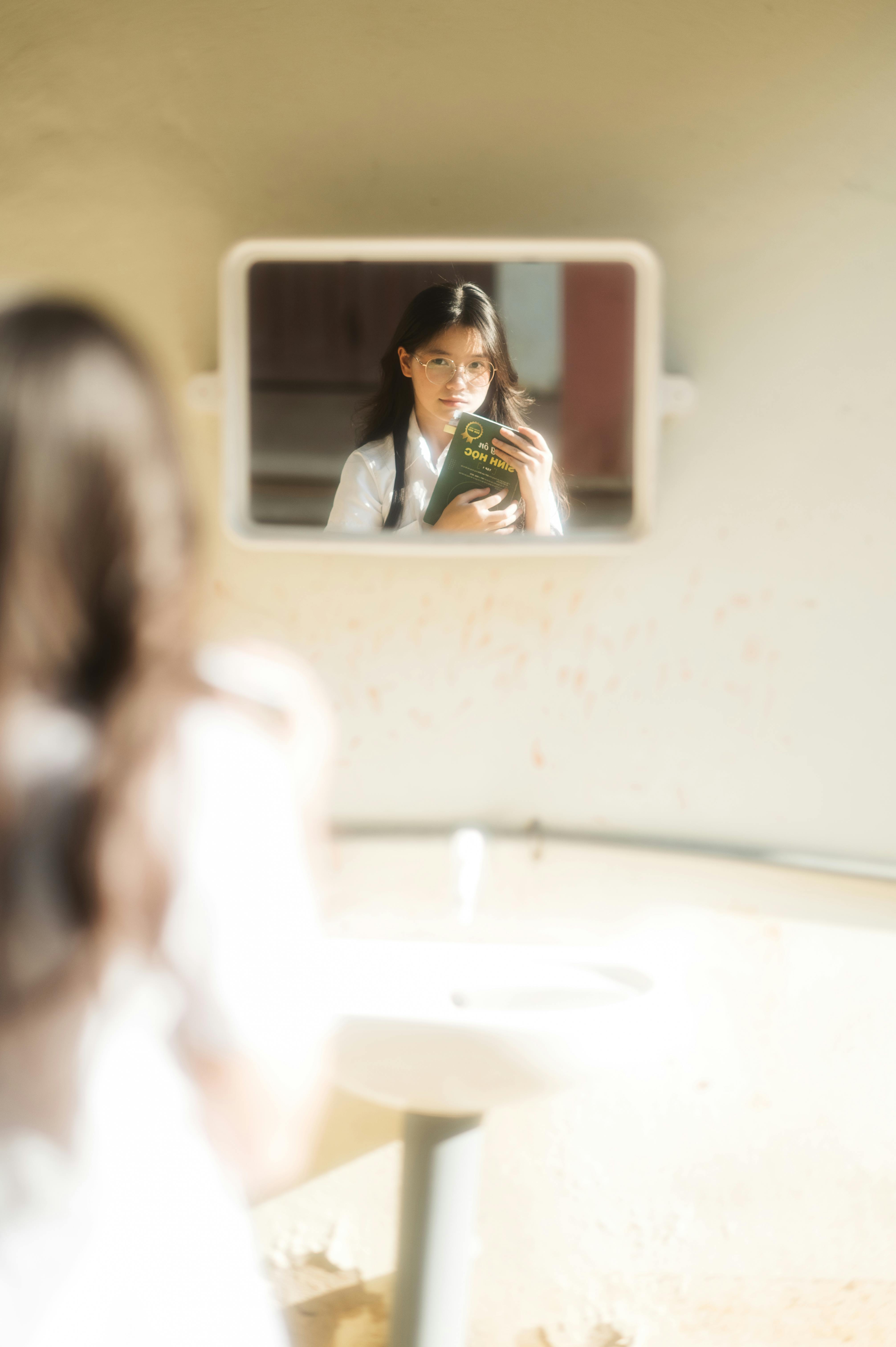 reflective adolescent girl holding book in mirror