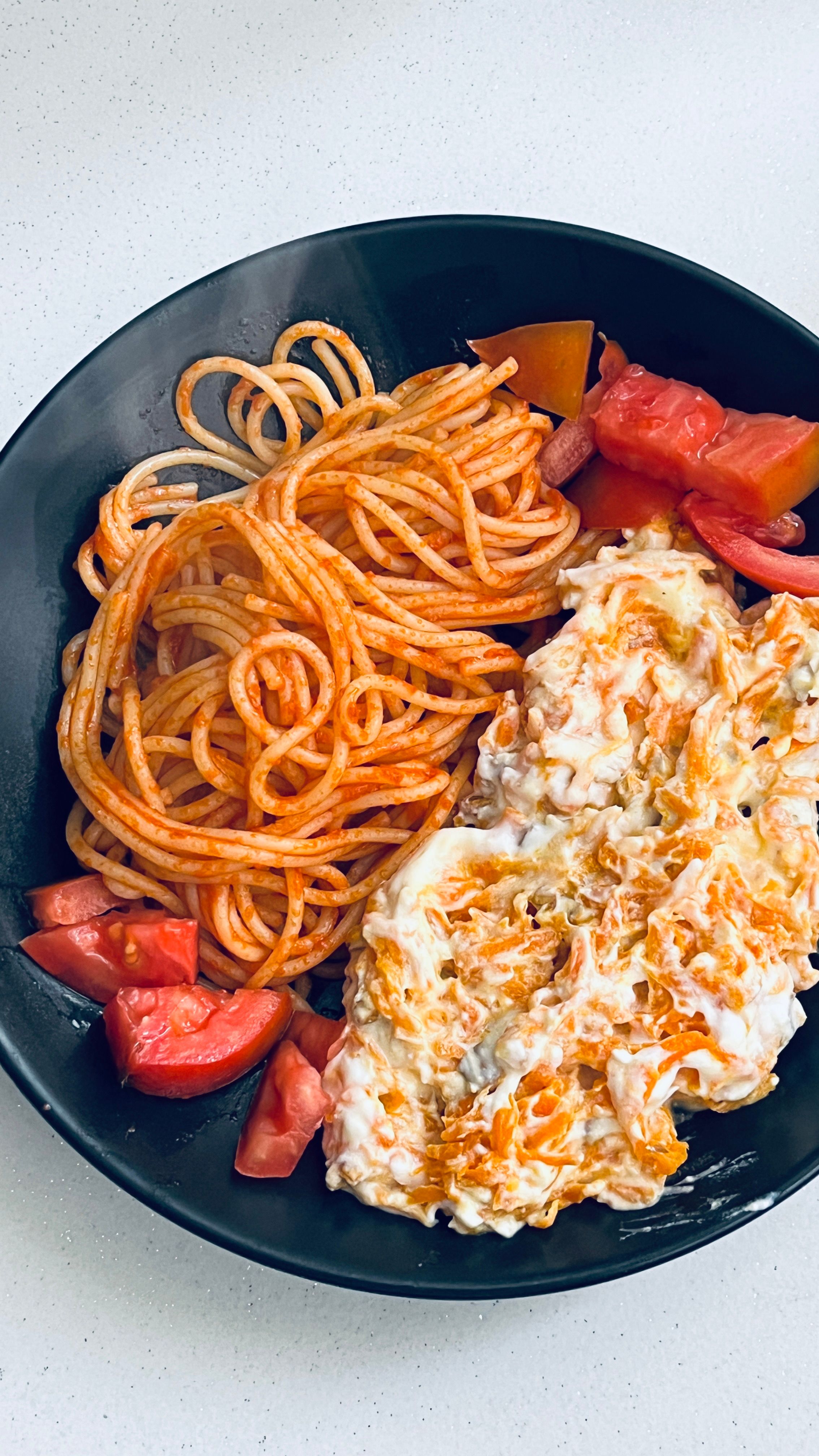 Plate of spaghetti with tomato slices and cheese, perfect for a hearty meal.