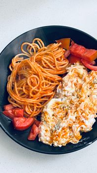 Plate of spaghetti with tomato slices and cheese, perfect for a hearty meal.