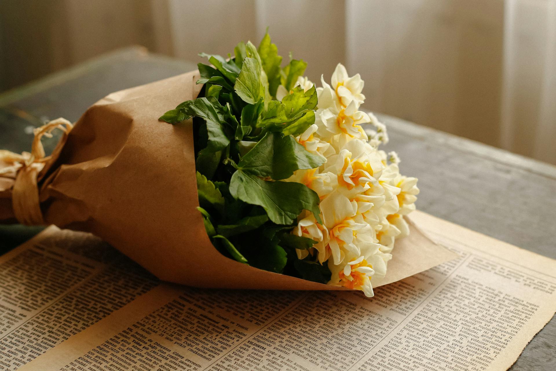 Delicate bouquet of daffodils wrapped in brown paper, resting on a vintage newspaper.