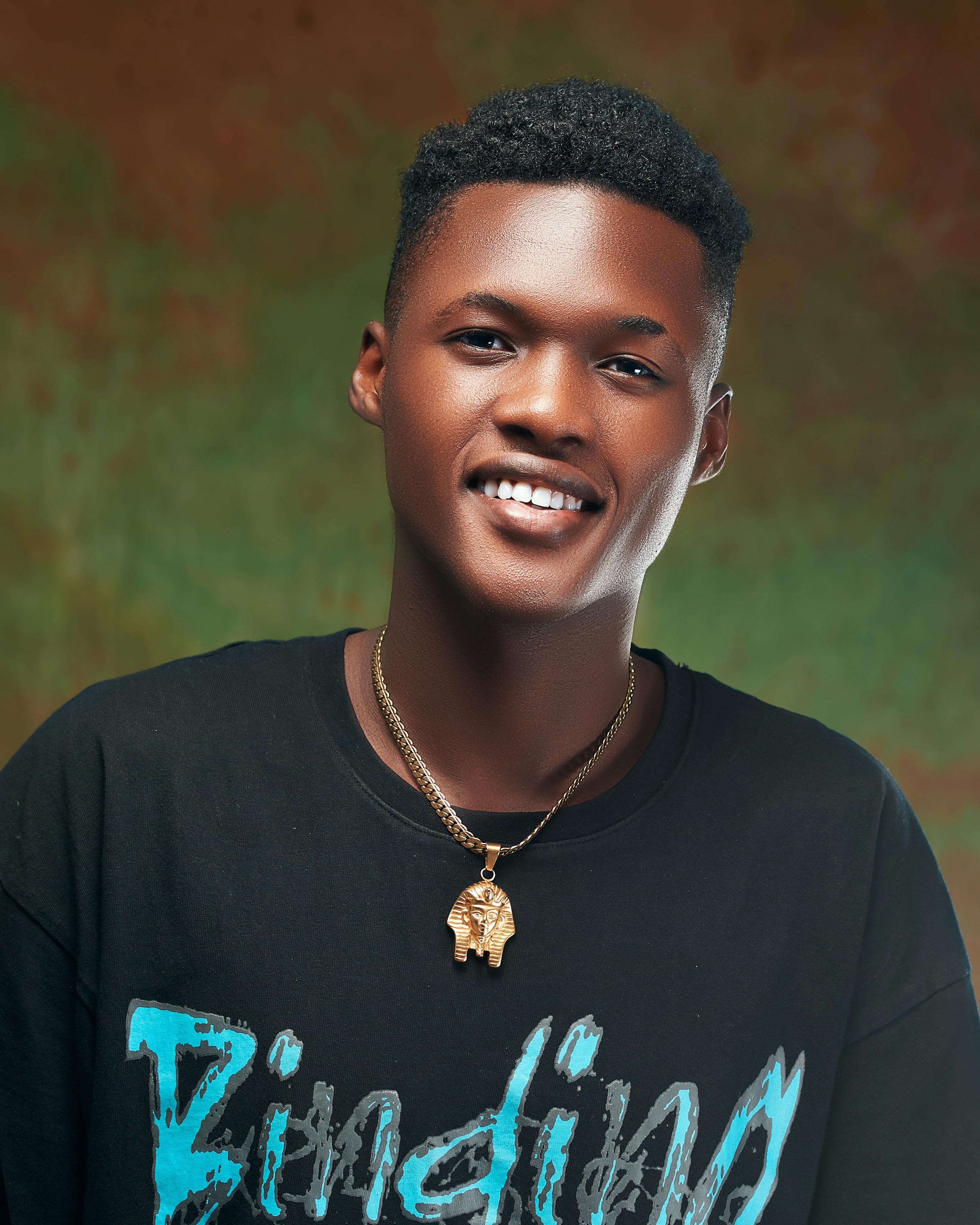 Portrait of a smiling young man wearing a stylish necklace against a textured background.