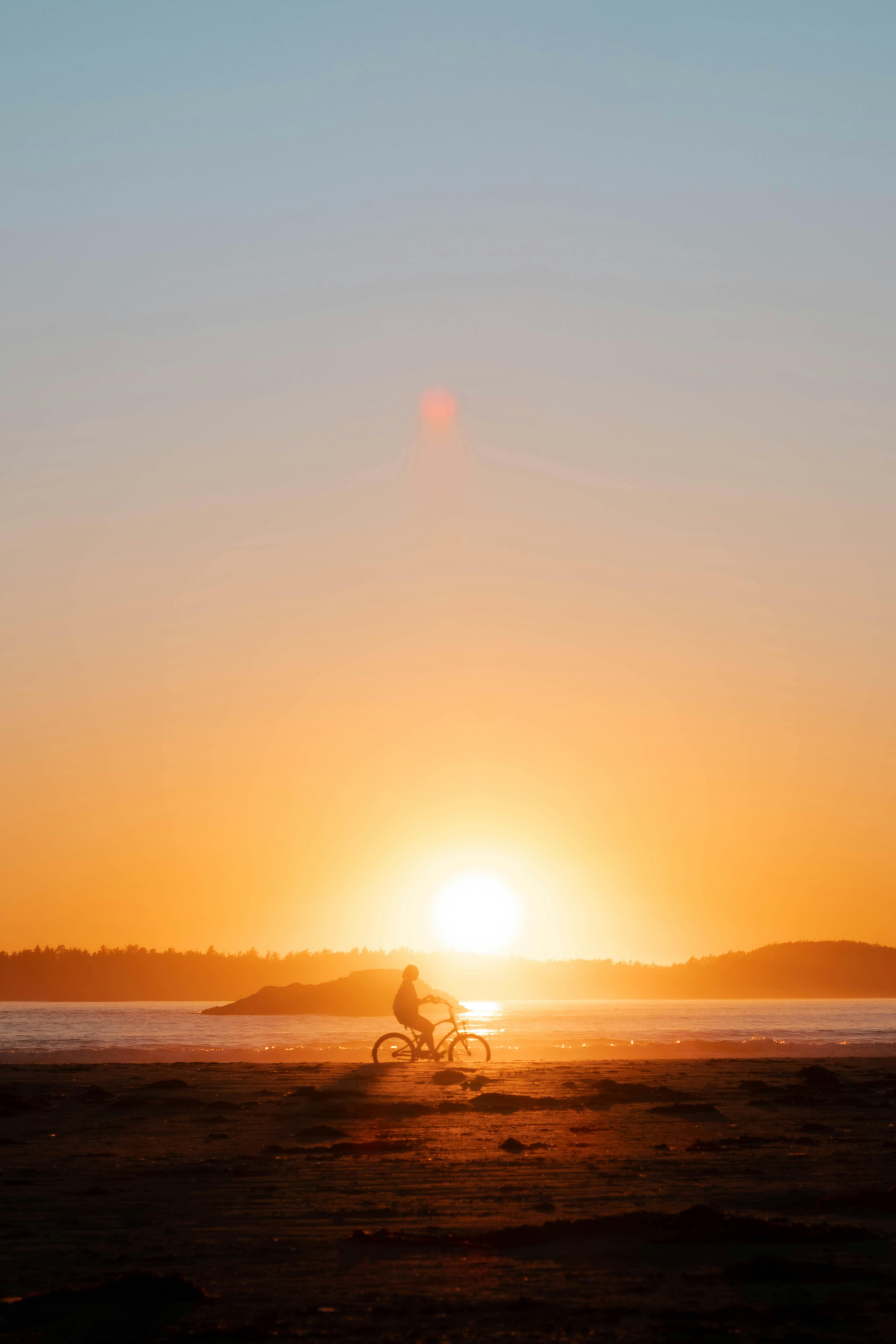 Silhouette of a cyclist at sunset on a sandy beach with vibrant colors.
