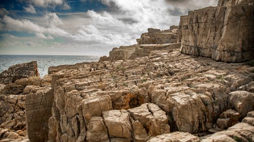 Free Dramatic coastal cliff with a rocky terrain against a blue sky and ocean backdrop. Stock Photo