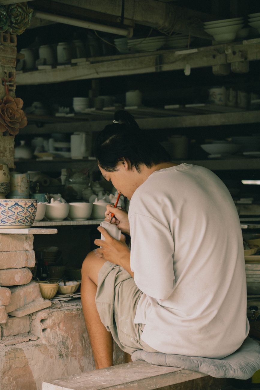 A potter skillfully decorates ceramics in a cozy, traditional workshop setting.