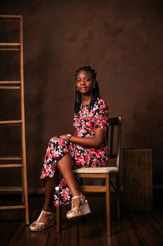 Studio portrait of a woman sitting gracefully on a chair wearing a floral dress.