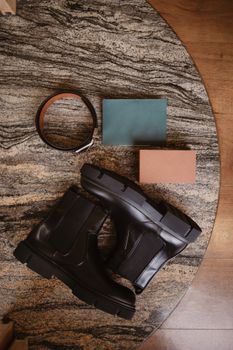Stylish black leather boots paired with belt and notebooks on a marble surface.