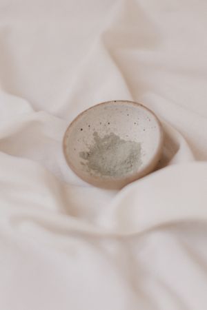 Bol d'argile verte en poudre avec une cuillère en bois, prêt pour un masque maison