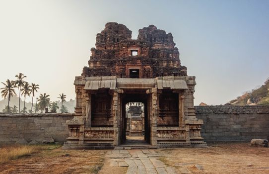 Majestic ancient temple ruins in Hampi, India, captured at sunrise with palm trees in the background.