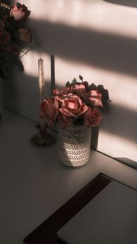 Pink roses in a vintage vase with sunlight streaming over a desk.