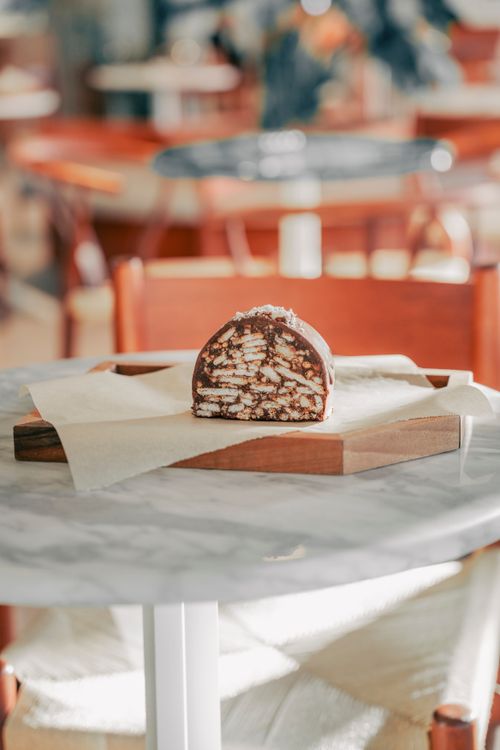 Free Close-up of a homemade chocolate biscuit cake slice displayed on a rustic wooden board in a cozy cafe setting. Stock Photo