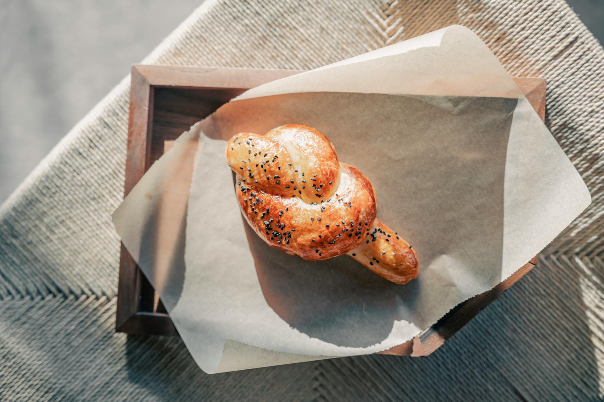 Artisanal knot-shaped bread with sesame seeds on baking paper in warm natural light.