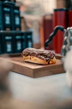 Chocolate eclair on wooden tray with blurred cafe background, perfect for dessert lovers.