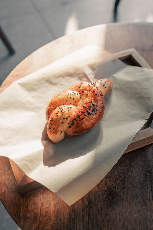 Free Close-up of a freshly baked soft pretzel topped with sesame seeds on parchment paper. Stock Photo