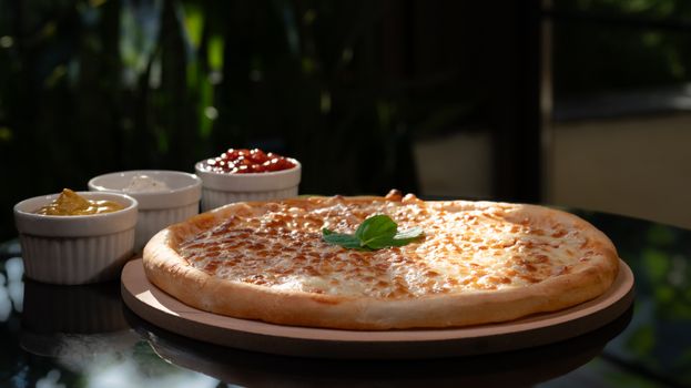 Mouthwatering cheese pizza with flavorful dips in natural light setting.
