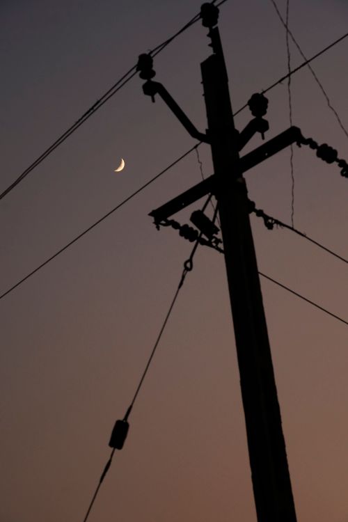 Free A crescent moon shines behind a silhouetted electrical pole at dusk, highlighting contrasts. Stock Photo