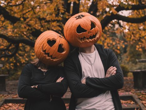 A creative Halloween-themed photo of a couple wearing pumpkin heads in a park during autumn.