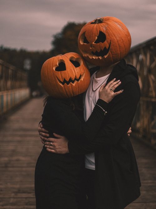 Free Creative Halloween-themed photo of a couple wearing pumpkin masks on a wooden bridge. Stock Photo