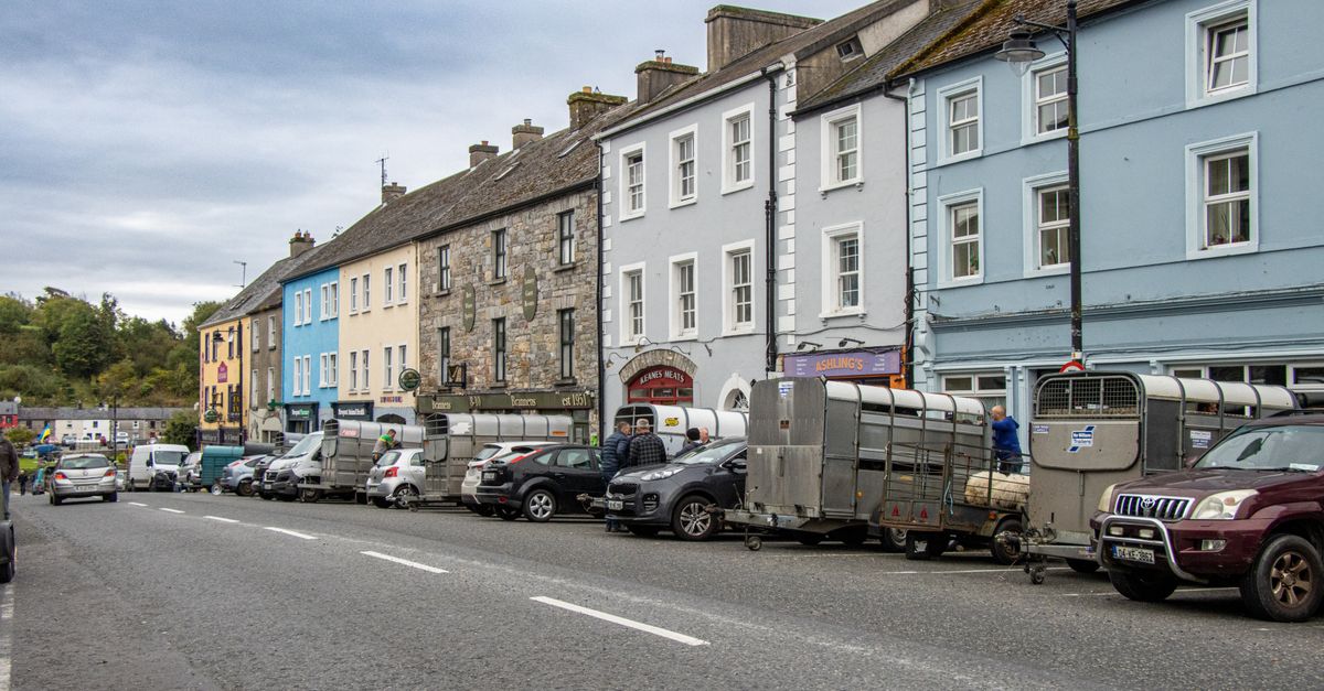 Street view of Kilkelly, Ireland showcasing colorful buildings and parked farming trailers along the road.