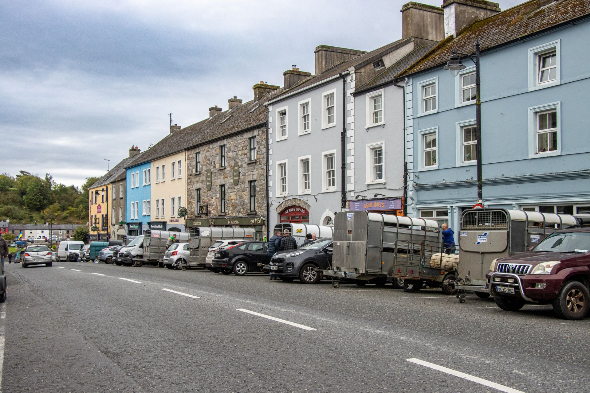 Street view of Kilkelly, Ireland showcasing colorful buildings and parked farming trailers along the road.