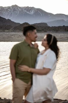 A couple embraces by a calm mountain lake at twilight, creating a romantic atmosphere.