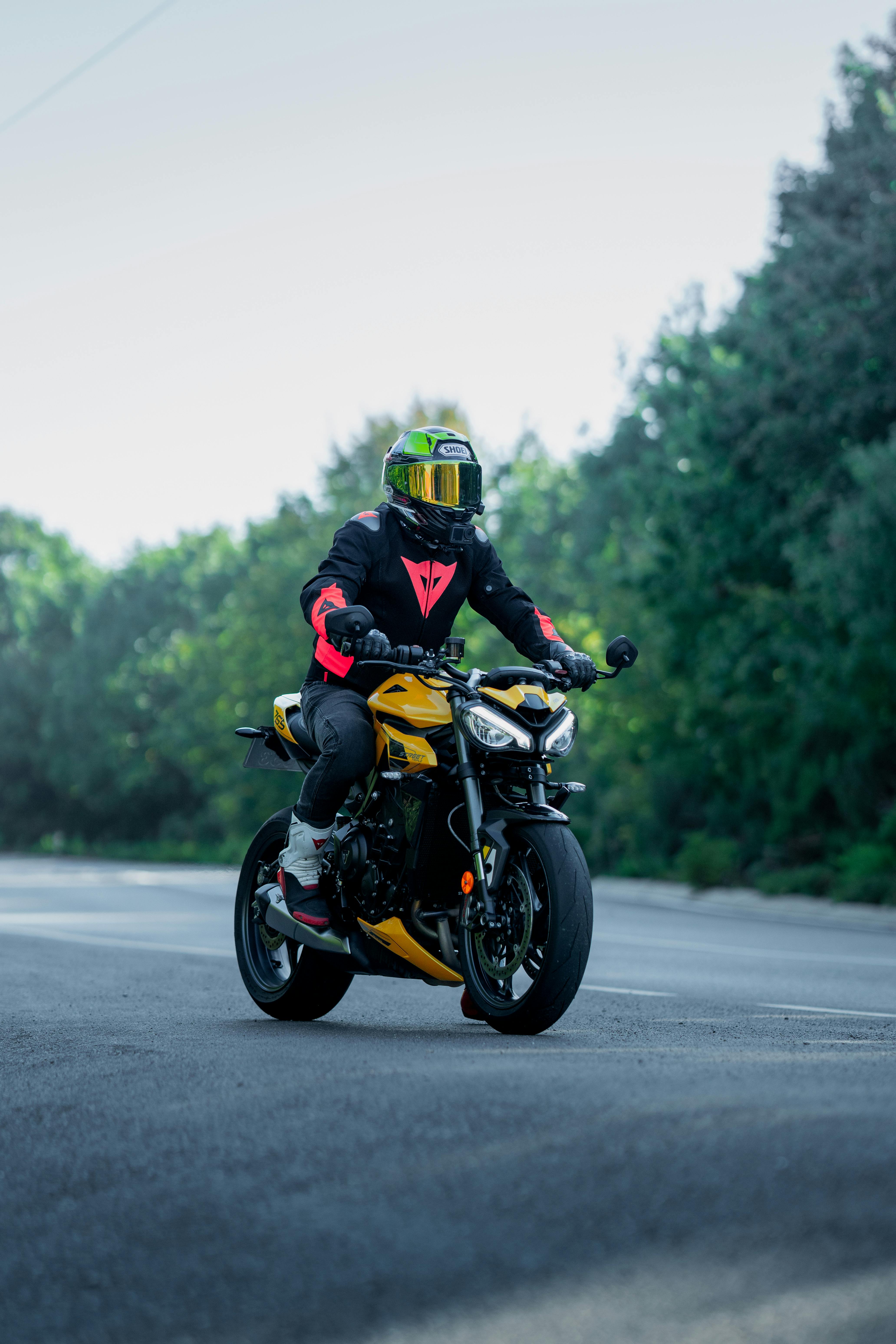 Motorcyclist wearing a helmet rides a yellow sports bike on a tree-lined road.