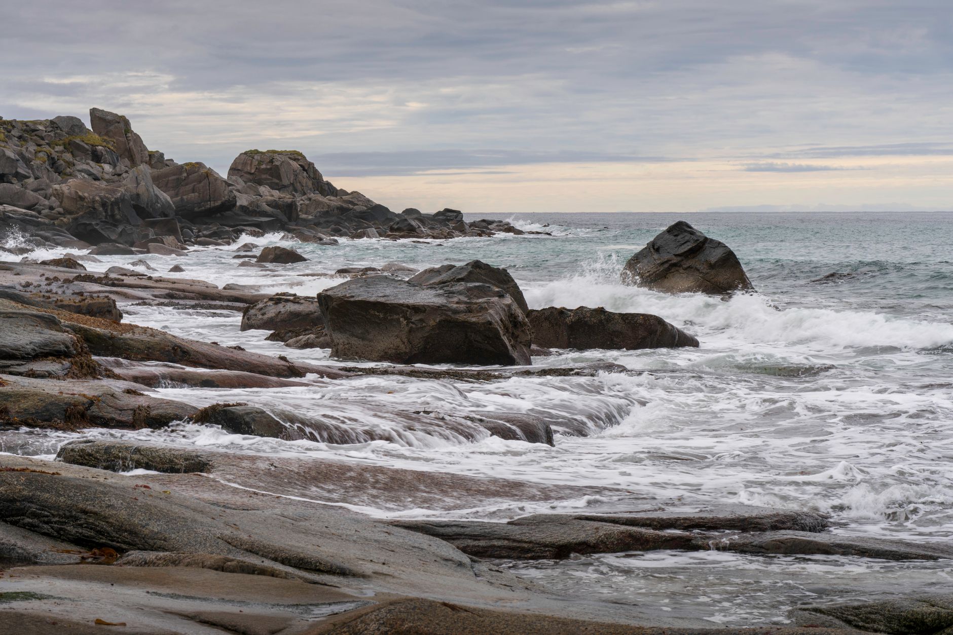 Serene coastal scene with waves crashing on rocky shore under cloudy skies.