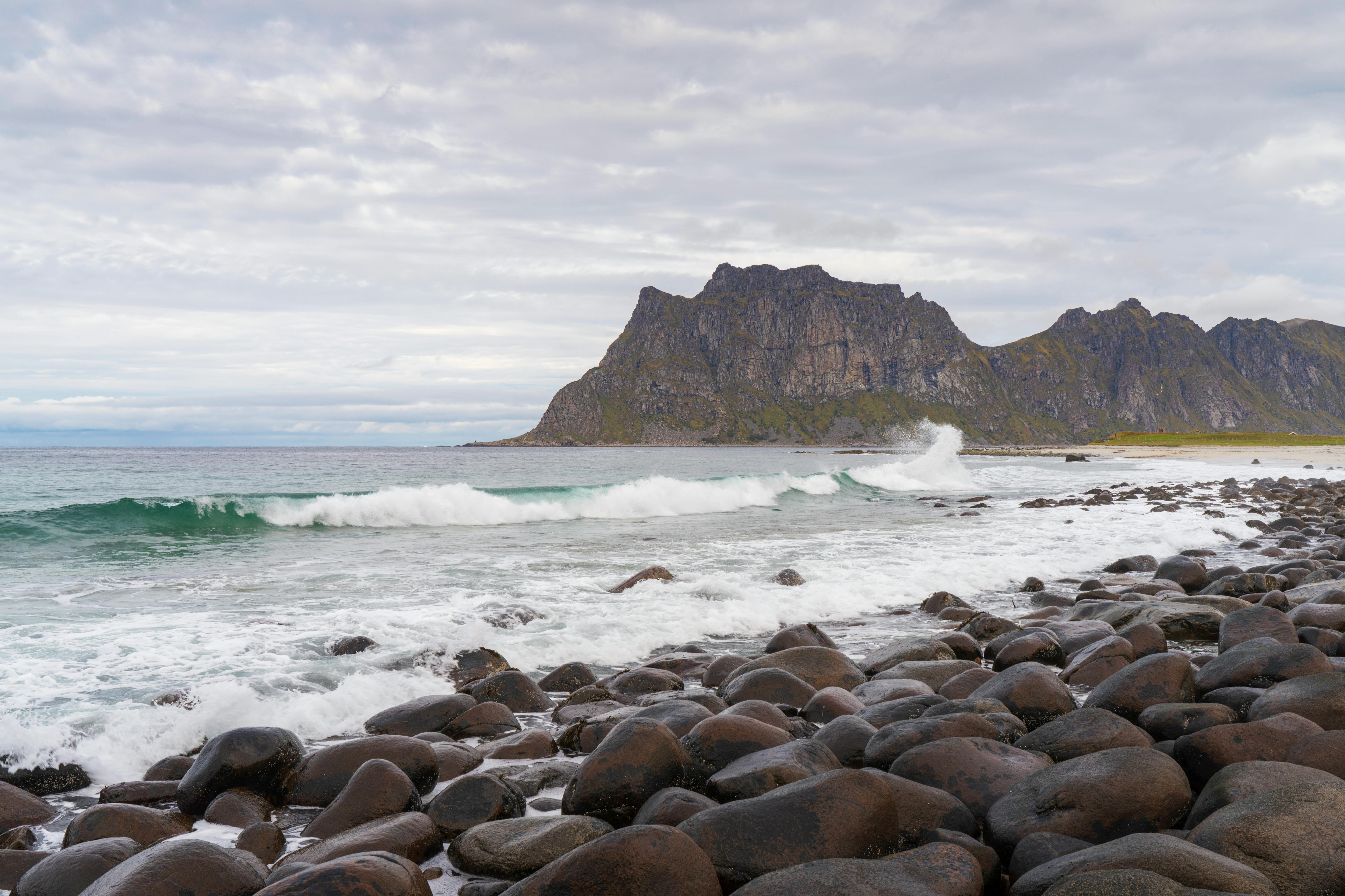 Serene rocky beach at Lofoten Islands, Norway, with waves crashing under a cloudy sky.