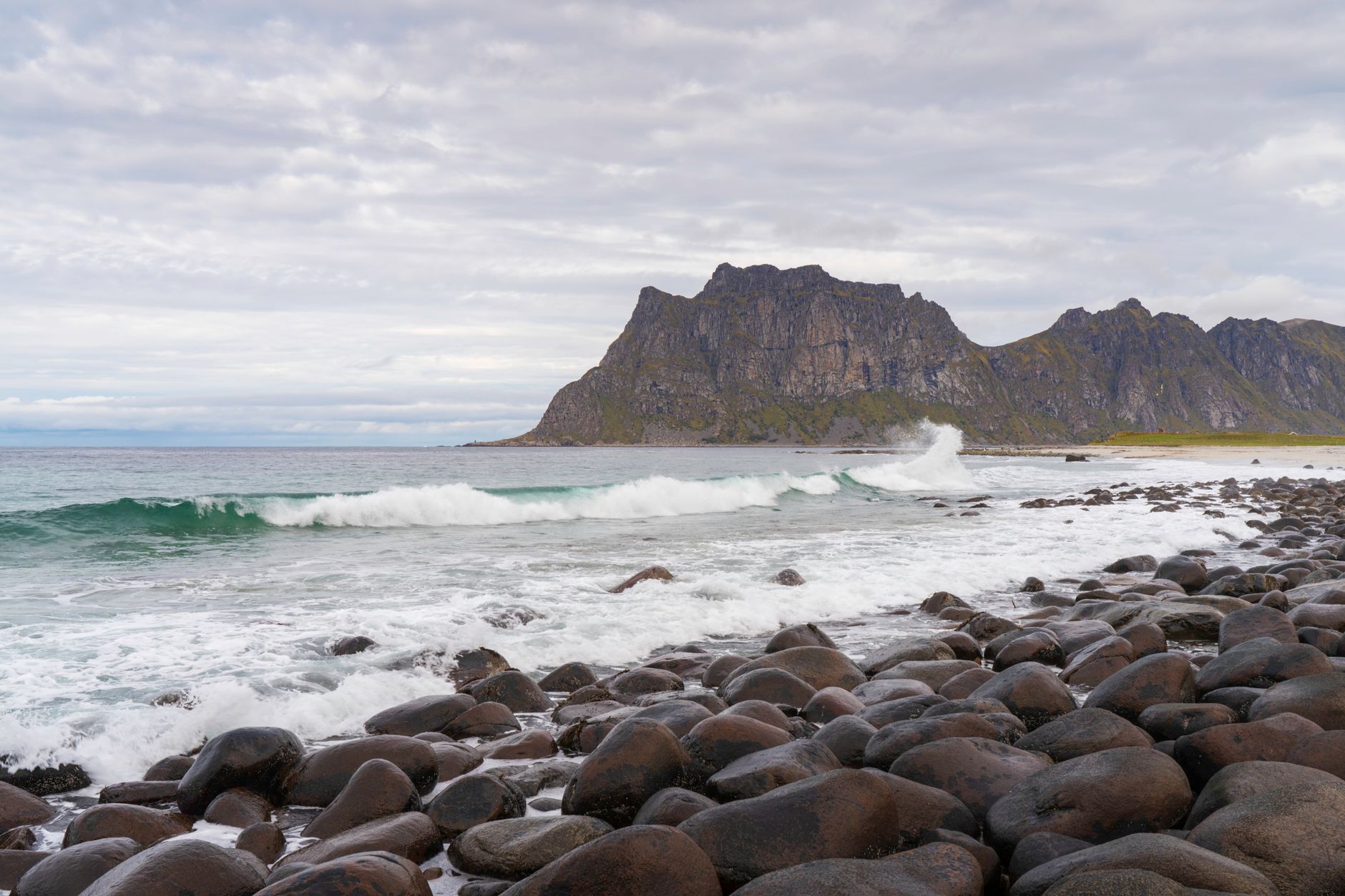 Serene rocky beach at Lofoten Islands, Norway, with waves crashing under a cloudy sky.