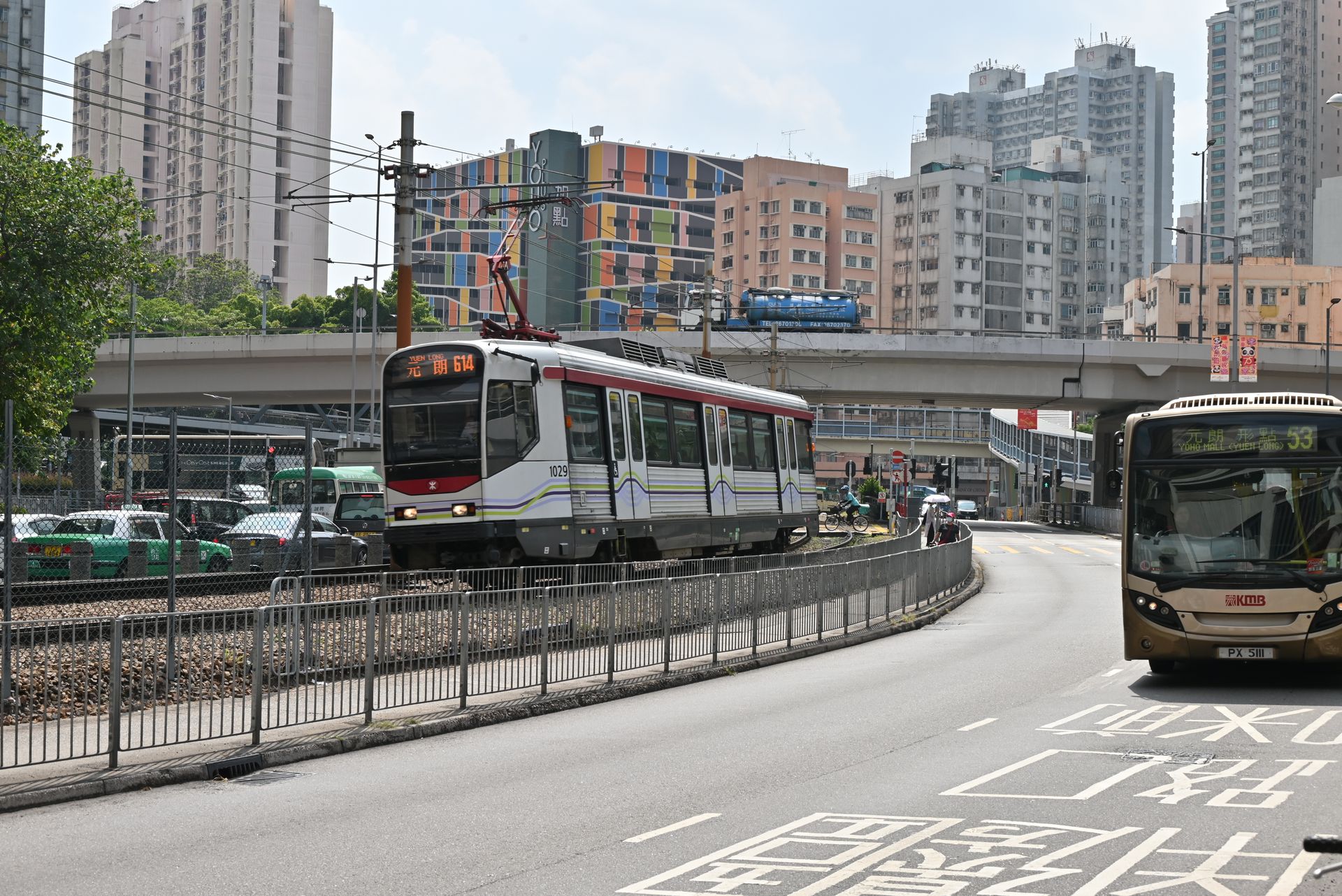 A city tram and bus navigate through a bustling urban environment with highrise buildings.