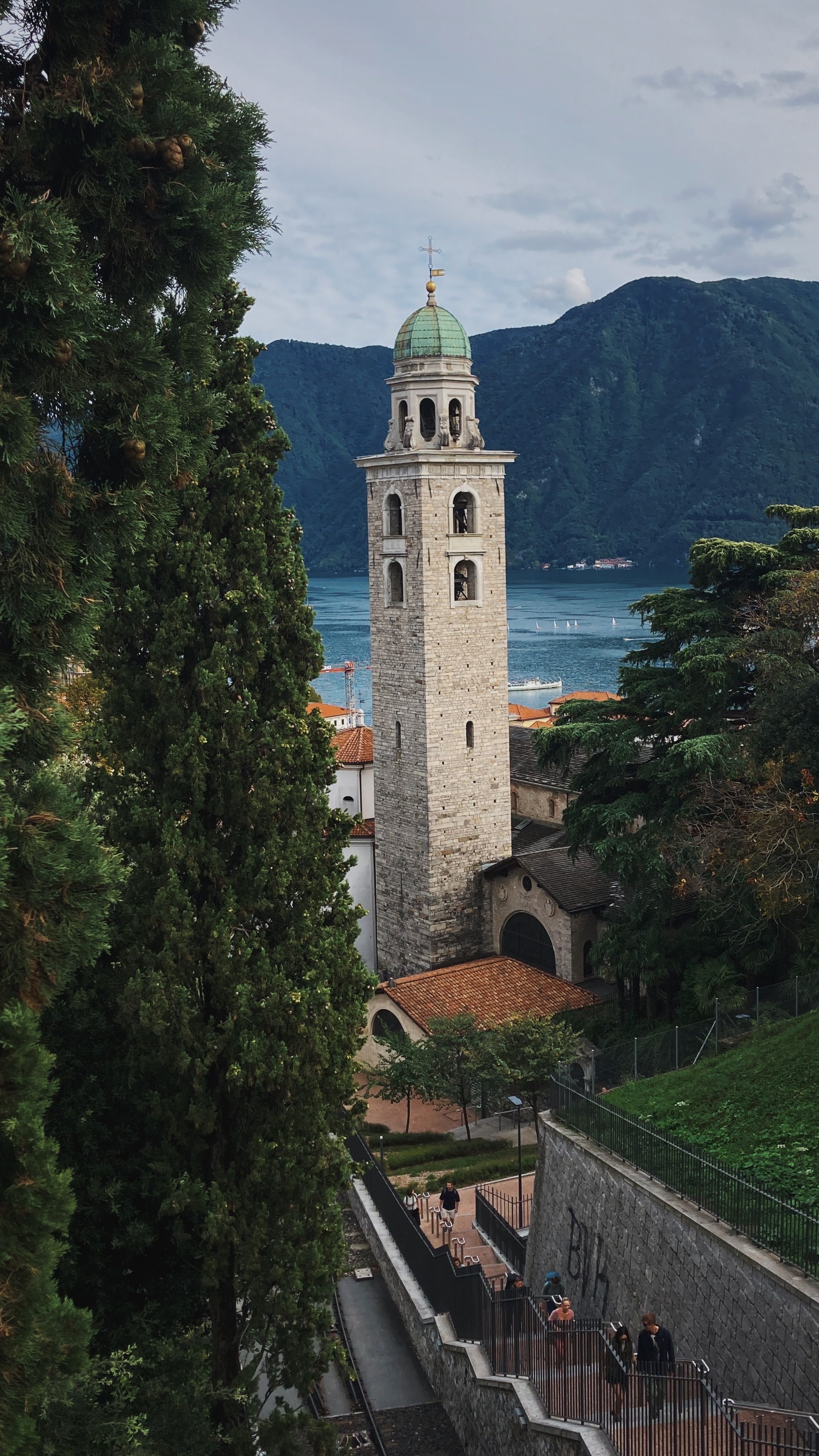Historic church tower amidst lush greenery and mountains near a serene lake.
