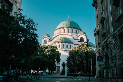 Free View of the iconic Saint Sava Temple in Belgrade on a sunny day, framed by trees and buildings. Stock Photo