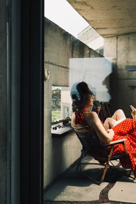 A woman in a red dress relaxes on a balcony in South Korea, embracing summer vibes.