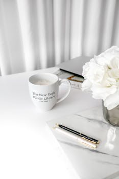 A minimalist workspace with a coffee mug, white flowers, and a notebook for an elegant touch.