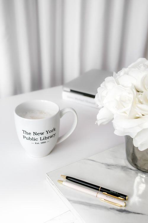 Free A white workspace featuring a mug, books, and white flowers in a metallic vase. Stock Photo