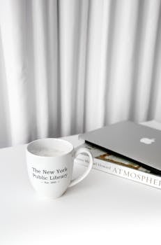 White mug with New York Public Library logo next to laptop on minimal desk.