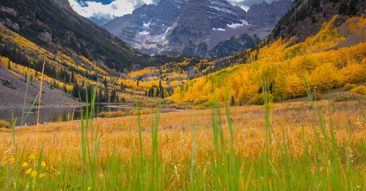 Vibrant fall colors surround Maroon Bells mountain, reflecting in alpine lake.