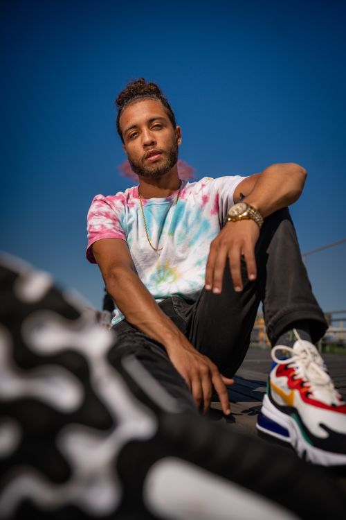 Free Stylish young man in tie-dye shirt and sneakers posing outdoors with a relaxed vibe. Stock Photo