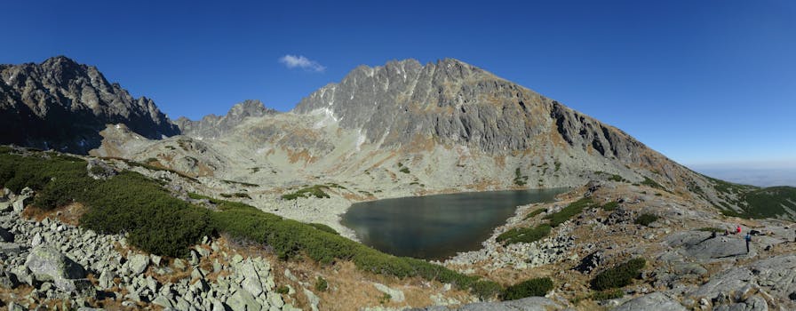 Breathtaking landscape of the High Tatras with a serene lake and rocky mountain peaks under a clear blue sky.