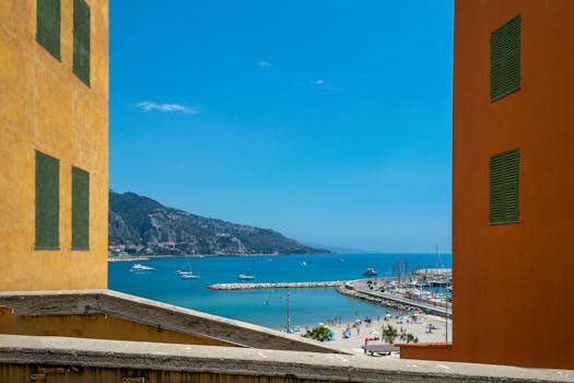 Vibrant cityscape of Menton with a stunning beach and marina view framed by colorful buildings. by Enrique Hoyos