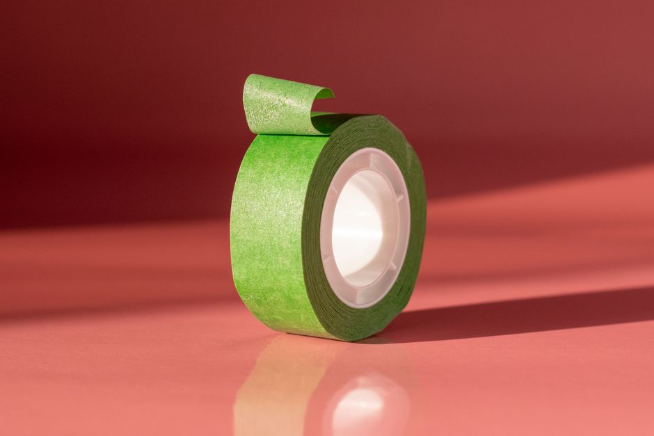 A roll of green tape stands out against a coral background in a minimalist setting.