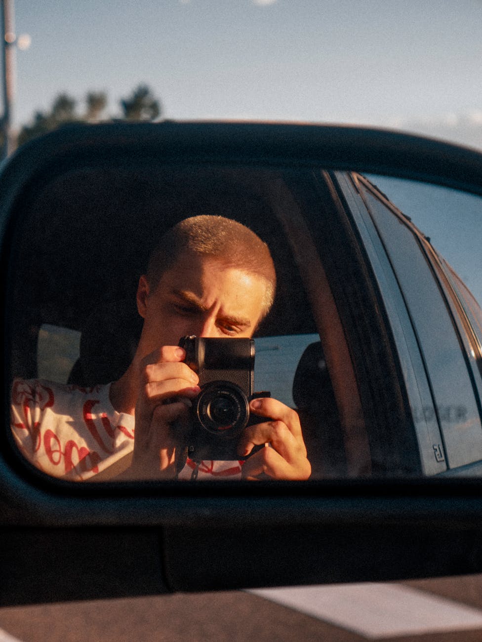 A photographer captures a self-portrait using a car's side mirror at golden hour.